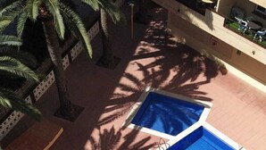 Uma piscina no terraço com superfície azul, rodeada por palmeiras e um deck revestido com azulejos.