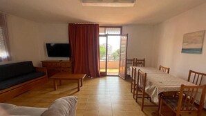 Sala de estar com sofá, televisão, mesa de jantar, cadeiras e porta de vidro deslizante para uma área externa.