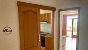 Uma porta de madeira dá acesso a uma cozinha com armários e bancada.