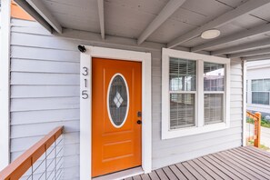 Ein Haus mit weißer Fassade, einer leuchtend orangefarbenen Tür mit der Nummer 315 und einem Fenster mit Jalousien.