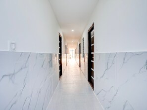 A long, narrow hallway with marble walls and doors, leading to a bright room at the end. - Deluxe Brookefield Central Bangalore Inn (Bengaluru)