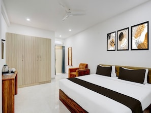 A hotel room with a bed, a wardrobe, a desk, a chair, and artwork on the wall. - Deluxe Brookefield Central Bangalore Inn (Bengaluru)