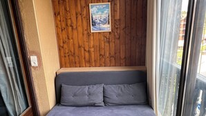 A wooden-paneled room with a grey sofa, a poster on the wall, and a window with a view of a building. - 4 bed apartment - La Joue du Loup (Dévoluy)