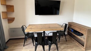 A dining area with a wooden table and black chairs, a TV mounted on the wall, and a wooden cabinet with a stove underneath. - 4 bed apartment - La Joue du Loup (Dévoluy)