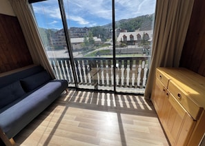 Ein Zimmer mit großem Fenster, Holzboden, einer Couch und einem Holzschrank.