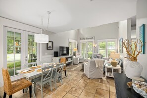 A spacious living area with a dining table, chairs, a sofa, and a television. - NEW to VRBO -HUGE PORCH~Golf Cart, FREE ACTIVITIES~HEATED Pool* & HotTub, Gym (Miramar Beach)