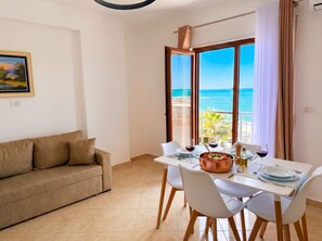 Un coin repas avec une table dressée pour deux personnes, un canapé et une vue sur la mer.