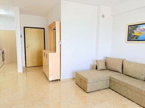 A living room with a beige sofa, a wooden cabinet, and a door leading to another room. - Sea View Apartment In Durres with Private Parking (Durres)
