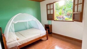 Quarto com teto de madeira, cama com mosquiteiro, janela com persianas e piso de azulejos.
