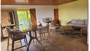 Uma sala de estar moderna com teto de madeira, área de jantar com mesa de vidro e um conjunto de sofá.