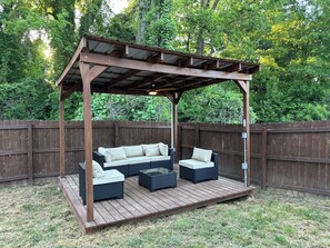 Une pergola en bois dotée d’un espace salon confortable, comprenant un canapé et deux fauteuils, installé sur une terrasse en bois.