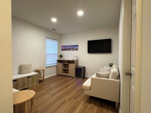 A living room with a sofa, a TV, a small table, a window with blinds, and a plant. - “Stylish 3BR Near NoDa w/ Outdoor Lounge" (Charlotte)