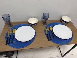 Ett matbord dukat med blå bordsunderlägg, vita tallrikar och guldfärgade bestick.