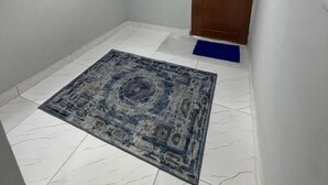 A hallway with a patterned rug, a wooden door, a window with a decorative grille, and a blue mat at the door entrance.