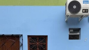 A building with a blue wall, a brown door, a window with a decorative grille, and an air conditioning unit.