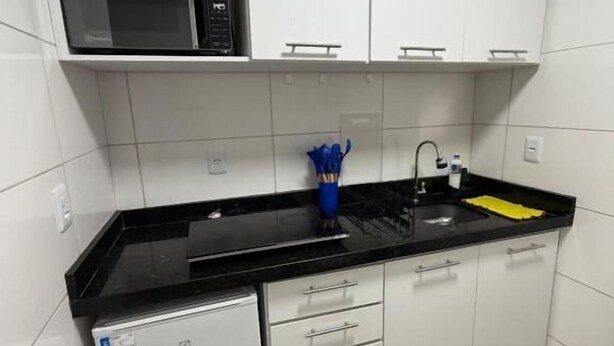 A compact kitchen with white cabinets, a black countertop, a small white dishwasher, and a sink with a yellow mat.