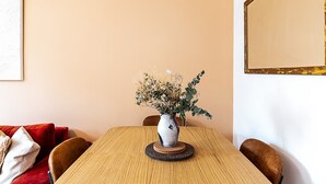 Ruokapöytä, jossa on maljakko täynnä kuivattuja kukkia, puinen tuoli ja punainen sohva.