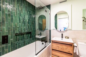 Ein modernes Badezimmer mit einer gläsernen Dusche, einem Holzausziehtisch und einer grünen Wandfliesen.