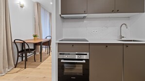 Ett kompakt kök med en inbyggd ugn, en diskho och en matplats med ett bord och stolar.