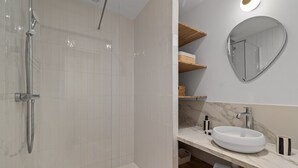 Ett modernt badrum med en dusch som är avskärmad med glasväggar, en vit tvättställ och en bänkskiva i marmor.