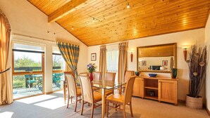 Un comedor con mesa de vidrio, sillas de madera, techo de madera y vista a la vegetación exterior.