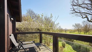 Terraza de madera con una mesa y sillas, con vistas a un paisaje verde con árboles.