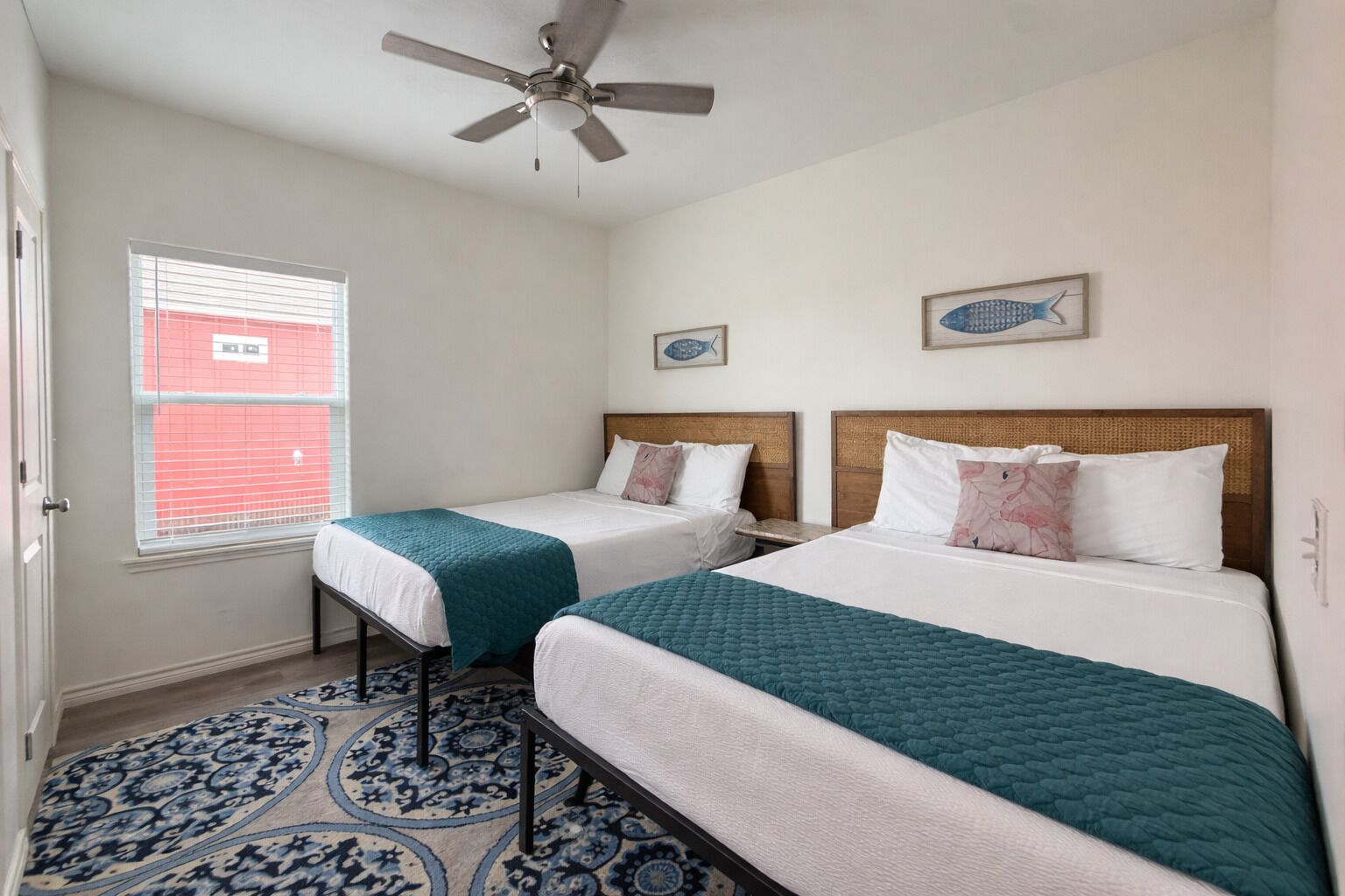 Ein Hotelzimmer mit zwei Betten, einem Deckenventilator, einem Fenster mit Jalousien und einem gemusterten Teppich.