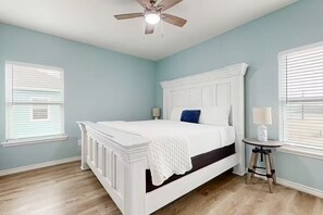 Ein Schlafzimmer mit einem weißen Bett, einem Deckenventilator und einem kleinen Tisch mit einer Lampe.