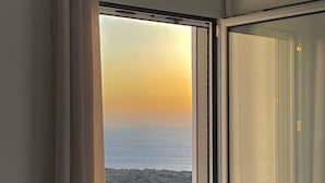 A room with a view of the sea at sunset, a window with curtains, and a sofa with cushions. - Eagle s Nest Kythnos (Kithnos)