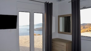 A room with a sliding glass door to a scenic outdoor area, a wooden dresser, and a mounted television. - Eagle s Nest Kythnos (Kithnos)