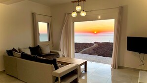 A living room with a sofa, a coffee table, a TV, and a view of the sunset over the sea. - Eagle s Nest Kythnos (Kithnos)
