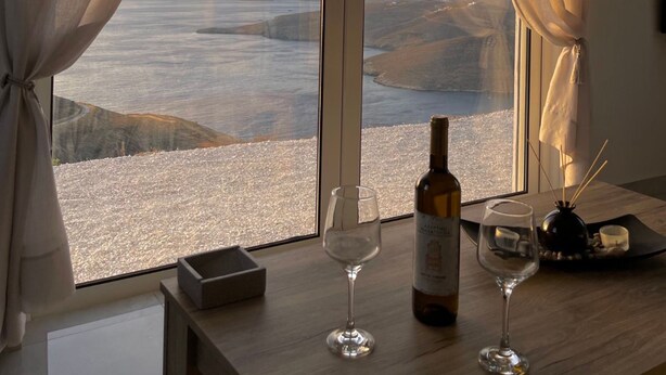 A room with a large window, a bottle of wine, and two glasses on a wooden table. - Eagle s Nest Kythnos (Kithnos)