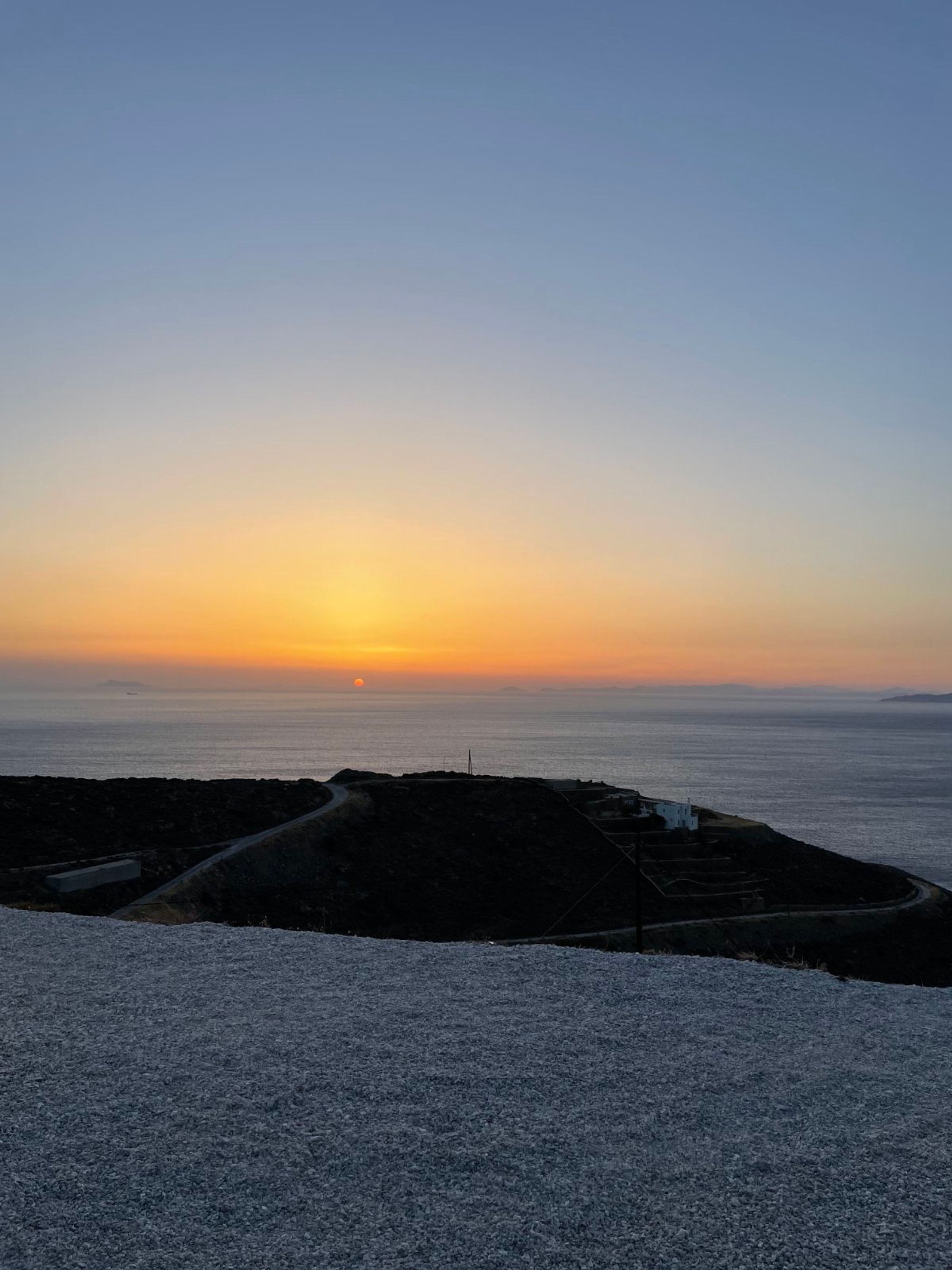A coastal landscape with a sunset, rocky terrain, and a small white building.