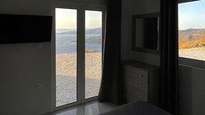 A bedroom with a bed, a TV, a wardrobe, and a large window with a view of the sea. - Eagle s Nest Kythnos (Kithnos)