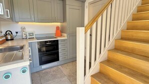 A kitchen with grey cabinets, a wooden staircase, and a stainless steel kettle. - Charming Barn Annex With Stables New Forest Escape (Ringwood)
