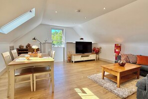Een ruime woonkamer met een eettafel, stoelen, een bank, salontafel, televisie en een groot raam.