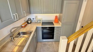 A compact kitchen with grey cabinets, a stainless steel sink, a built-in oven, and a small countertop area. - Charming Barn Annex With Stables New Forest Escape (Ringwood)