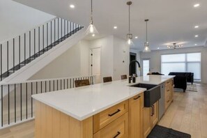 A modern kitchen with a central island, wooden cabinets, and a staircase with a glass railing. - Chic Retreat 4 BR Near UofC & HWY , Free Parking (Calgary)