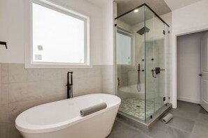 A modern bathroom with a freestanding bathtub, a glass-enclosed shower, and a window providing natural light.