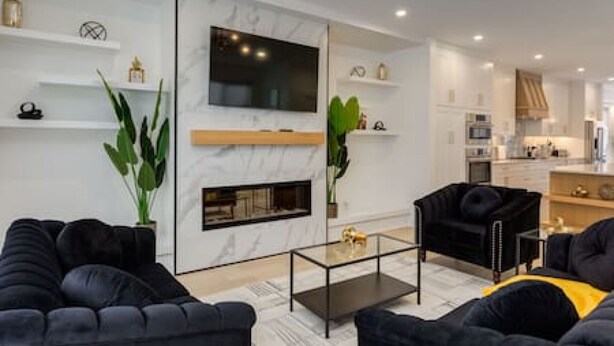 A modern living room with a fireplace, black sofas, a glass coffee table, and a TV mounted on the wall. - Chic Retreat 4 BR Near UofC & HWY , Free Parking (Calgary)