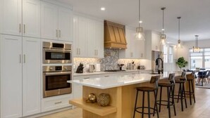 A modern kitchen with white cabinetry, stainless steel appliances, a large island with bar stools, and pendant lighting. - Chic Retreat 4 BR Near UofC & HWY , Free Parking (Calgary)