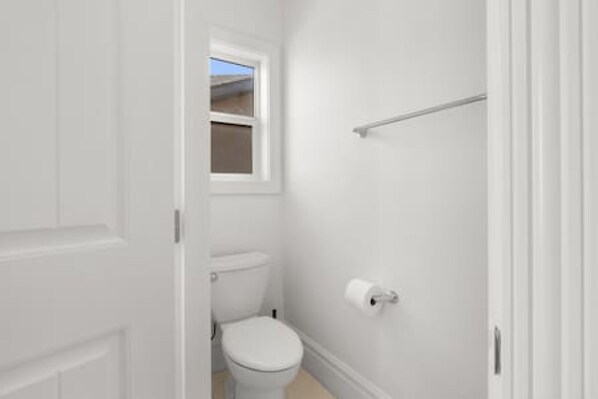 Un baño pequeño y blanco con inodoro, ventana y toallero.