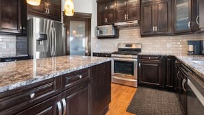 A modern kitchen with dark wood cabinets, stainless steel appliances, and a granite countertop. - "Amantara" 5 BR Luxury Retreat | Bright & Serene (Calgary)