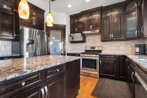 A modern kitchen with dark wood cabinets, stainless steel appliances, and a granite countertop. - "Amantara" 5 BR Luxury Retreat | Bright & Serene (Calgary)