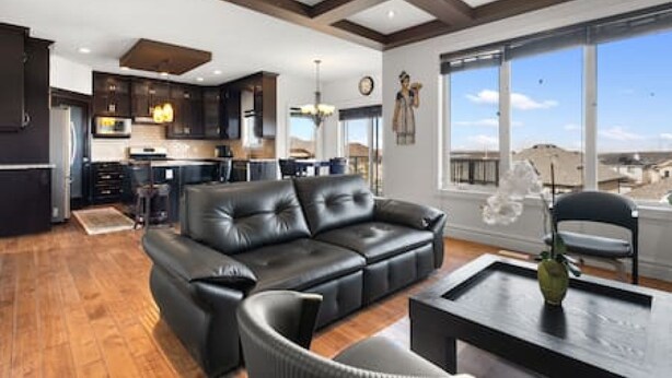 A spacious living area with a black leather sofa, a dining table, and a large window offering a view of the landscape. - "Amantara" 5 BR Luxury Retreat | Bright & Serene (Calgary)
