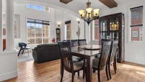 A dining area with a wooden table and chairs, a chandelier, and large windows. - "Amantara" 5 BR Luxury Retreat | Bright & Serene (Calgary)