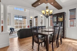 A dining area with a wooden table and chairs, a chandelier, and large windows. - "Amantara" 5 BR Luxury Retreat | Bright & Serene (Calgary)