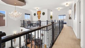 A spacious hallway with a high ceiling, a chandelier, and a balcony with a railing. - "Amantara" 5 BR Luxury Retreat | Bright & Serene (Calgary)