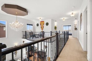A spacious hallway with a high ceiling, a chandelier, and a balcony with a railing. - "Amantara" 5 BR Luxury Retreat | Bright & Serene (Calgary)