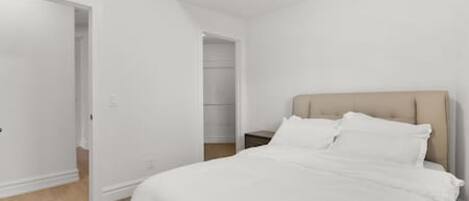 A bedroom with a bed, a nightstand, and a door leading to another room.